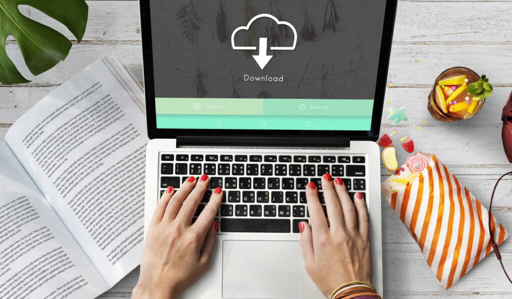 Hands typing on a laptop with a download icon on screen